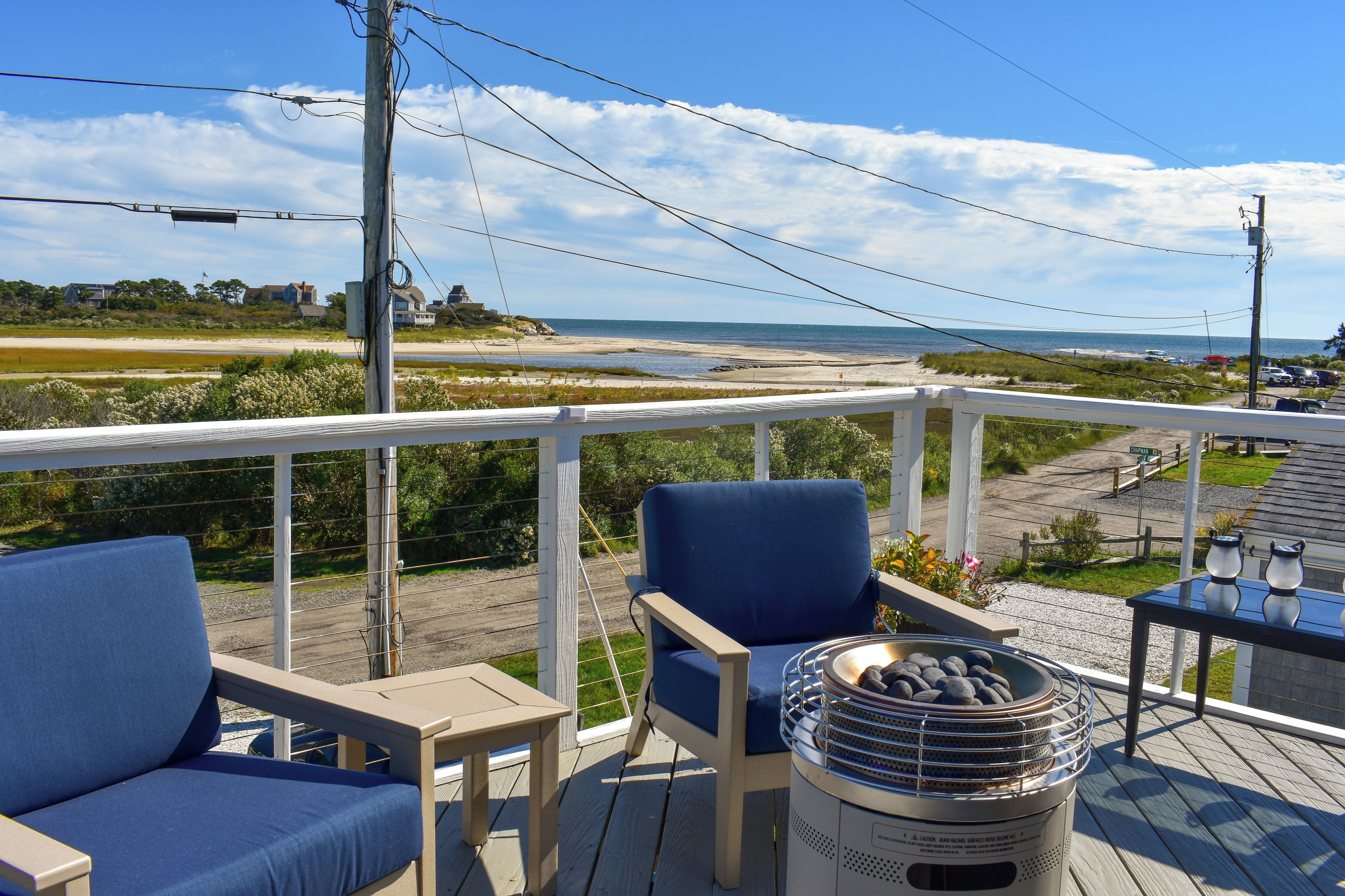 A deck with two chairs and a table, overlooking a beach and ocean.