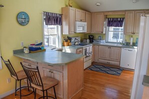 A kitchen with wooden cabinets, a microwave, a stove, a sink, and a clock on the wall.