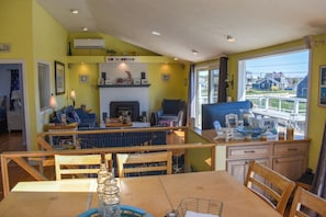 A dining area with a wooden table, chairs, and a view of the beach through large windows.