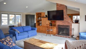 Un soggiorno con camino, divani blu, un tavolino in legno e una TV a parete.