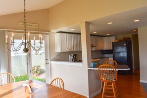 Una cocina con armarios blancos, un refrigerador negro y un comedor con sillas de madera y una mesa.