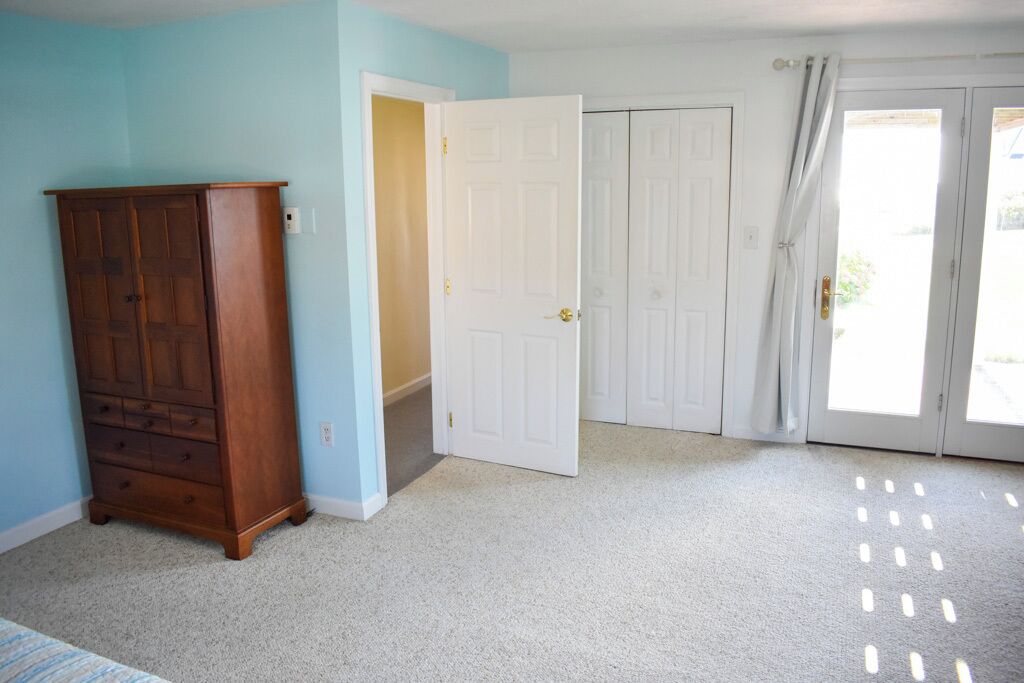 A room with a wooden wardrobe, a white door, and a sliding glass door leading outside.