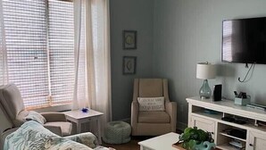 A living room with a sofa, armchair, coffee table, TV, and a window with blinds. - Charming, Chic, Right Next to the Beach (Santa Rosa Beach)