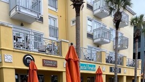Outdoor seating with yellow chairs and orange umbrellas in front of a building with balconies and signs for 'Sunrise Coffee Co.' and 'Coastal Paradise'. - Charming, Chic, Right Next to the Beach (Santa Rosa Beach)