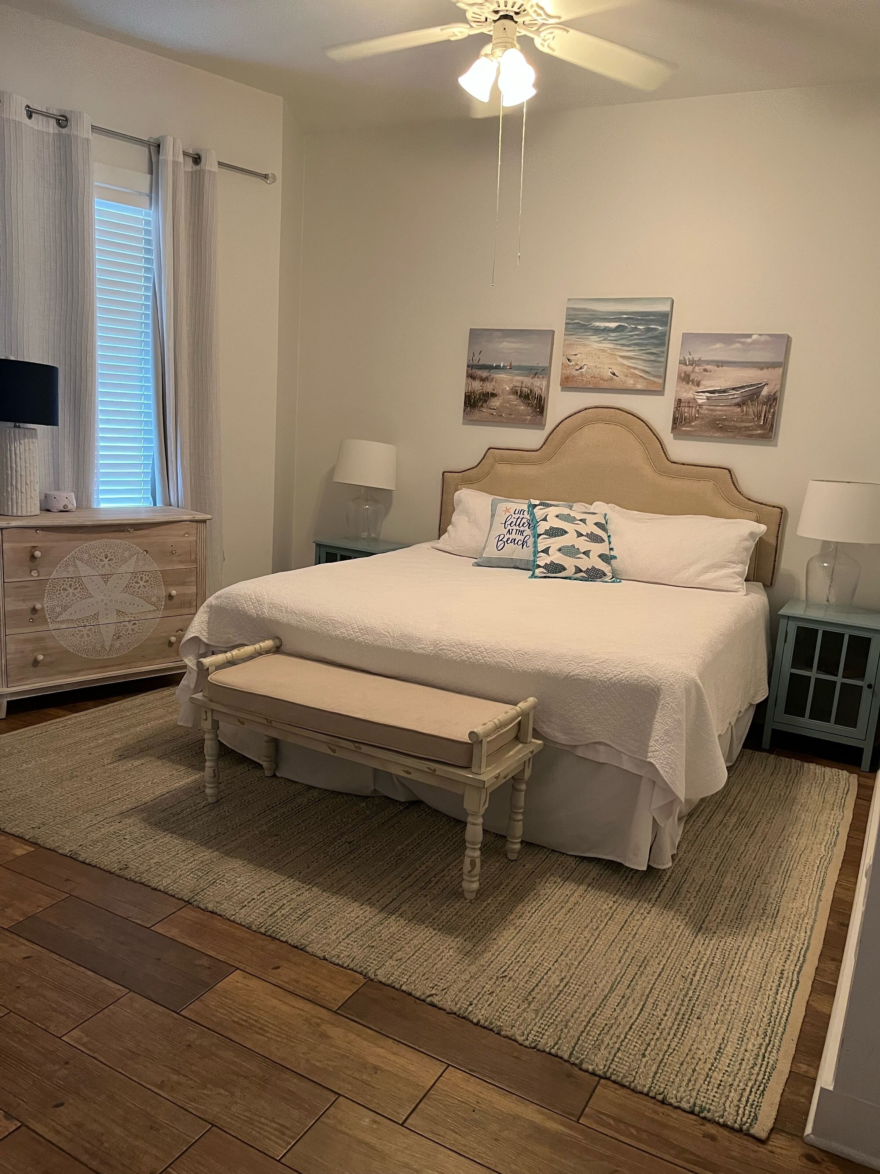 Un dormitorio con cama, mesitas de noche, ventilador de techo y obras de arte en la pared.