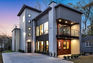 A modern two-story house with a balcony, large windows, and a well-lit entrance.