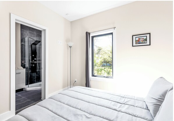 A bedroom with a bed, a window with a view, and a bathroom with a shower.