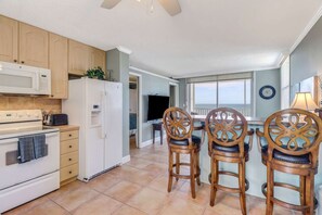 A kitchen with a stove, microwave, refrigerator, and wooden chairs. - DIRECT GULF VIEW | 10TH FLOOR BALCONY |  KING BED | FREE PARKING | STEPS TO BONITA BEACH (Bonita Springs)