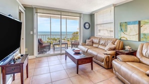 A living room with a large TV, leather sofas, a coffee table, and a view of the ocean through a sliding glass door. - DIRECT GULF VIEW | 10TH FLOOR BALCONY |  KING BED | FREE PARKING | STEPS TO BONITA BEACH (Bonita Springs)