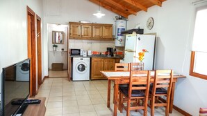 A compact kitchen with wooden cabinets, a refrigerator, a microwave, and a washing machine. - Cabañas Las Cumbres (El Calafate)