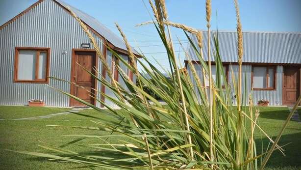 A building with a corrugated metal exterior and a sloped roof, featuring two wooden doors and windows. - Cabañas Las Cumbres (El Calafate)