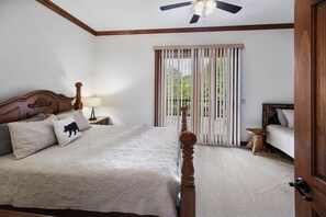 Ein Schlafzimmer mit Himmelbett, Nachttisch mit Lampe, Holzstuhl und Blick durch eine Schiebetür auf einen Außenbereich.
