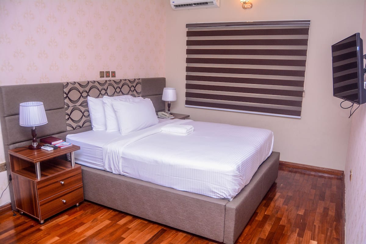 A neatly made bed with a headboard, a bedside table with a lamp, and a wall-mounted TV.
