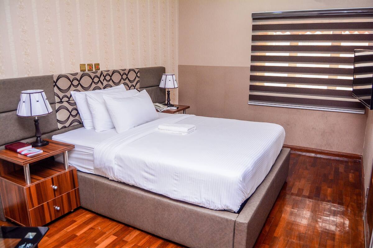 A neatly made bed with white linens, a wooden nightstand with a lamp, and a bedside table with a book.