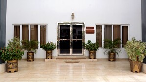 Ingresso di un hotel con porta in vetro, piante in vaso e cartello di benvenuto.