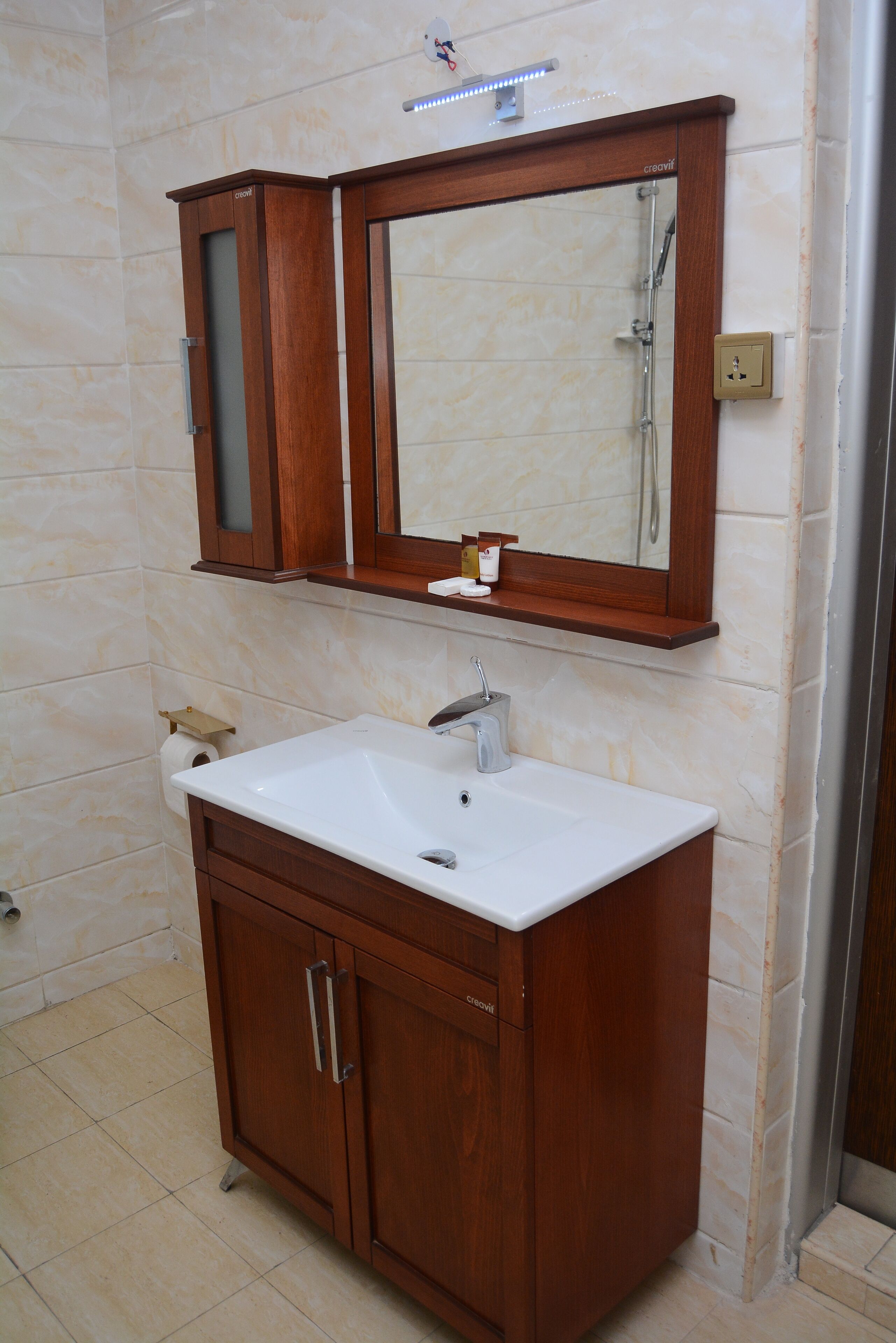 A bathroom with a wooden vanity, a white sink, a mirror, and a shower.
