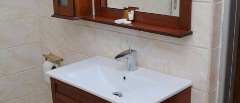 Un baño con tocador de madera, un lavabo blanco, un espejo y una ducha.