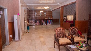 Una hall con una reception, sedie in legno, un tavolino con un'esposizione floreale e un orologio a parete.