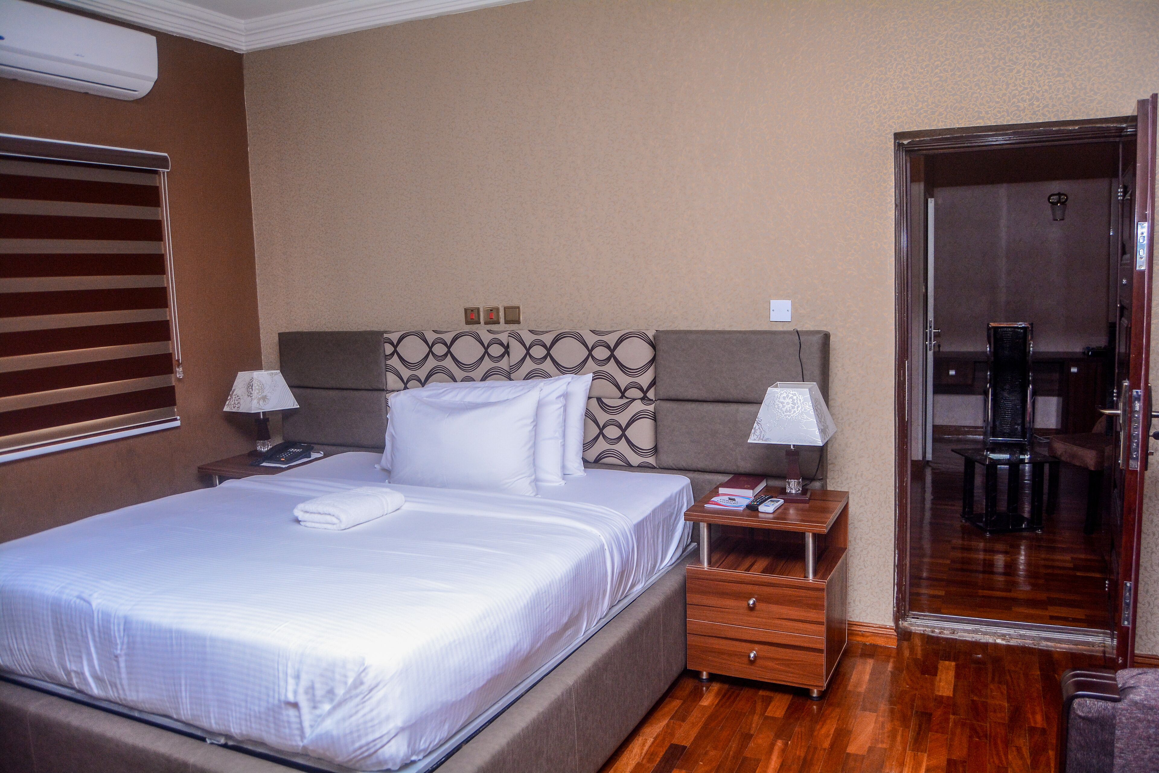 A hotel room with a large bed, two bedside tables with lamps, a wooden floor, and a sliding door leading to a bathroom.