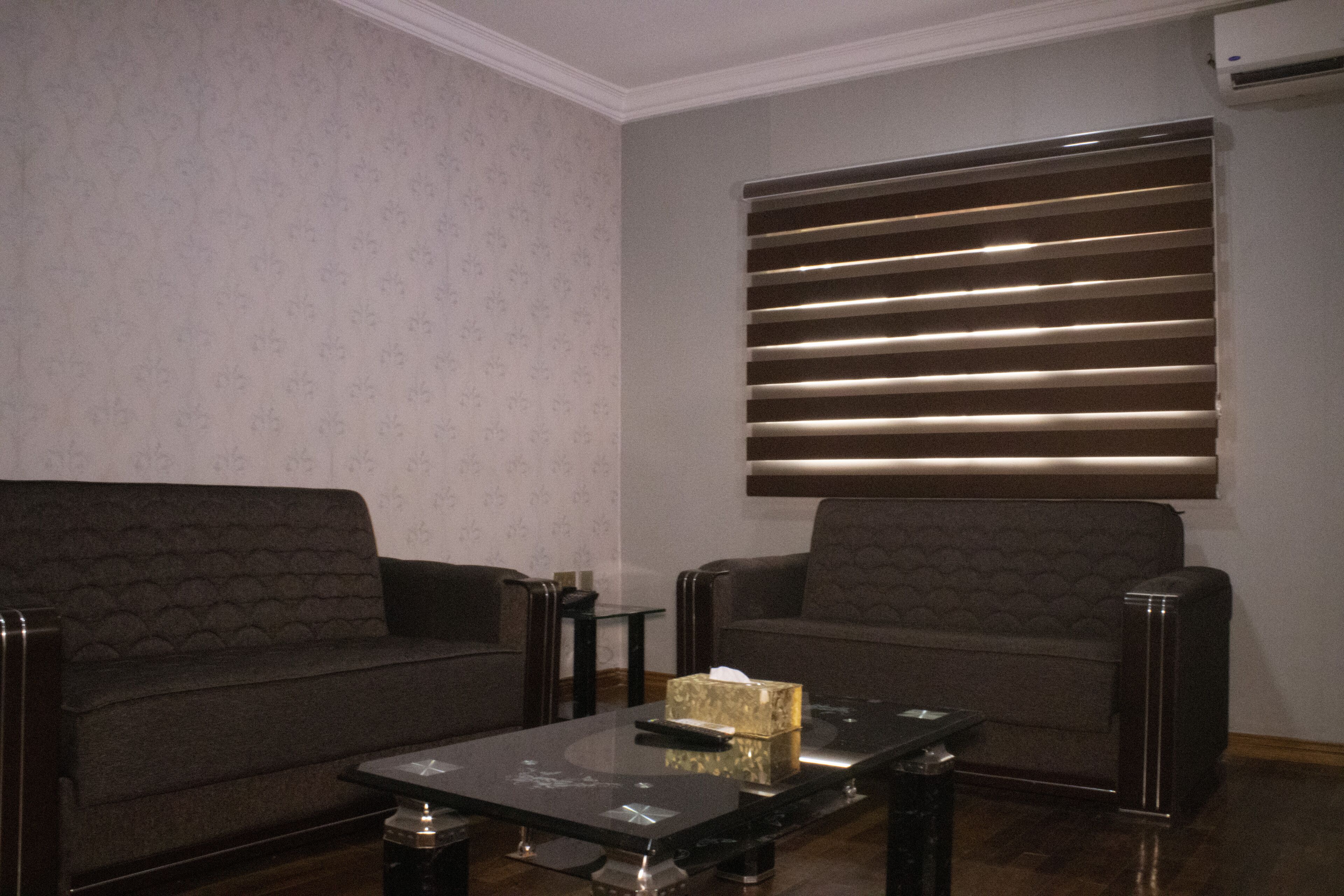 Uma sala de estar com dois sofás, uma mesa de centro e um aparelho de ar condicionado fixado na parede.