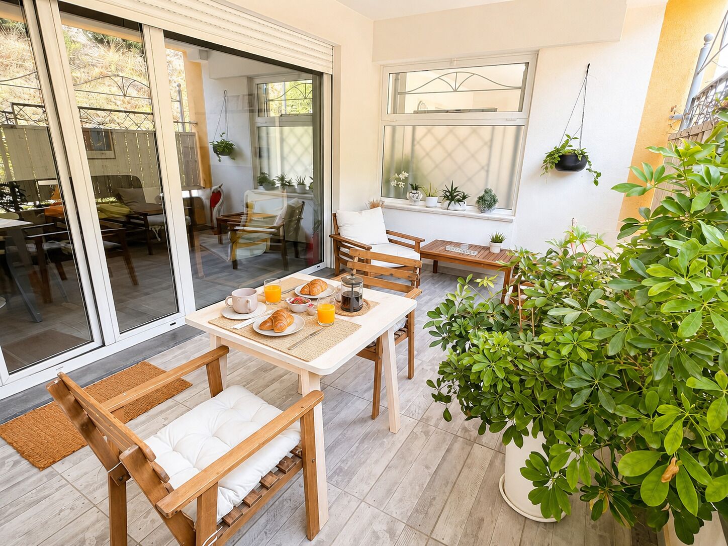 Un coin repas avec une table mise pour le petit-déjeuner, comprenant des croissants, du jus d’orange et du café. On y trouve des chaises et un banc avec des coussins.