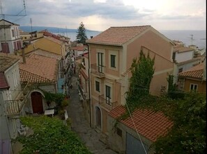 Uma rua estreita com edifícios em ambos os lados, com varandas e vista para o mar ao fundo.