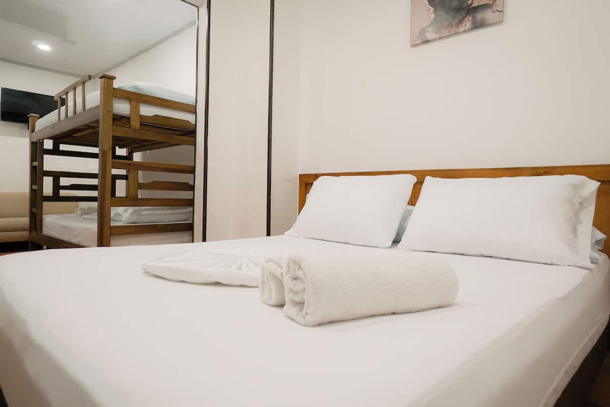 A single bed with white bedding and a neatly folded towel. A bunk bed is visible in the background.