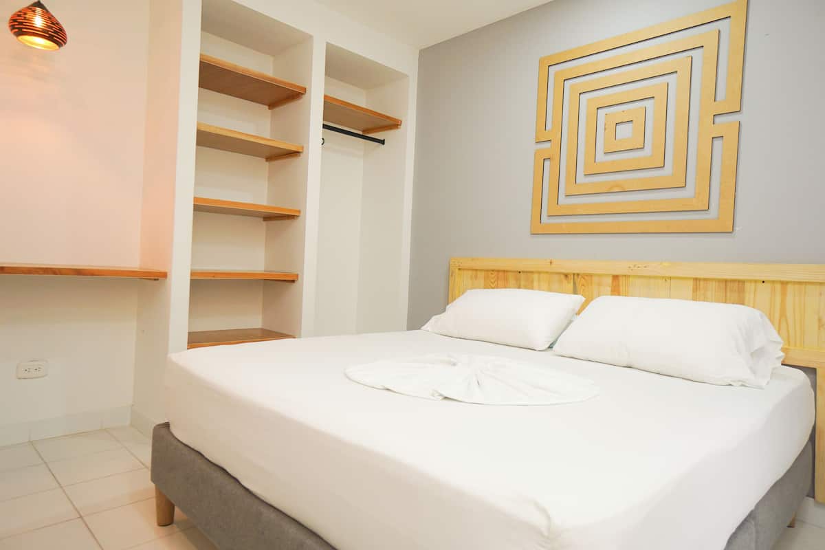 A neatly made bed with a wooden headboard, a wall-mounted geometric art piece, and built-in shelving units.