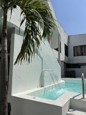 A pool area with a water feature, a palm tree, and a white building structure. - Paraiso Tayrona Casa de Playa (Santa Marta)