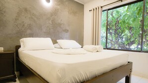 A neatly made bed with white linens and pillows, a wooden headboard, and a window with curtains. - Hostal Paraiso Tayrona (Santa Marta)