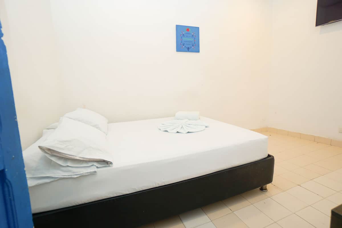 A single bed with white bedding and a folded towel, a blue sign on the wall, and a tiled floor.