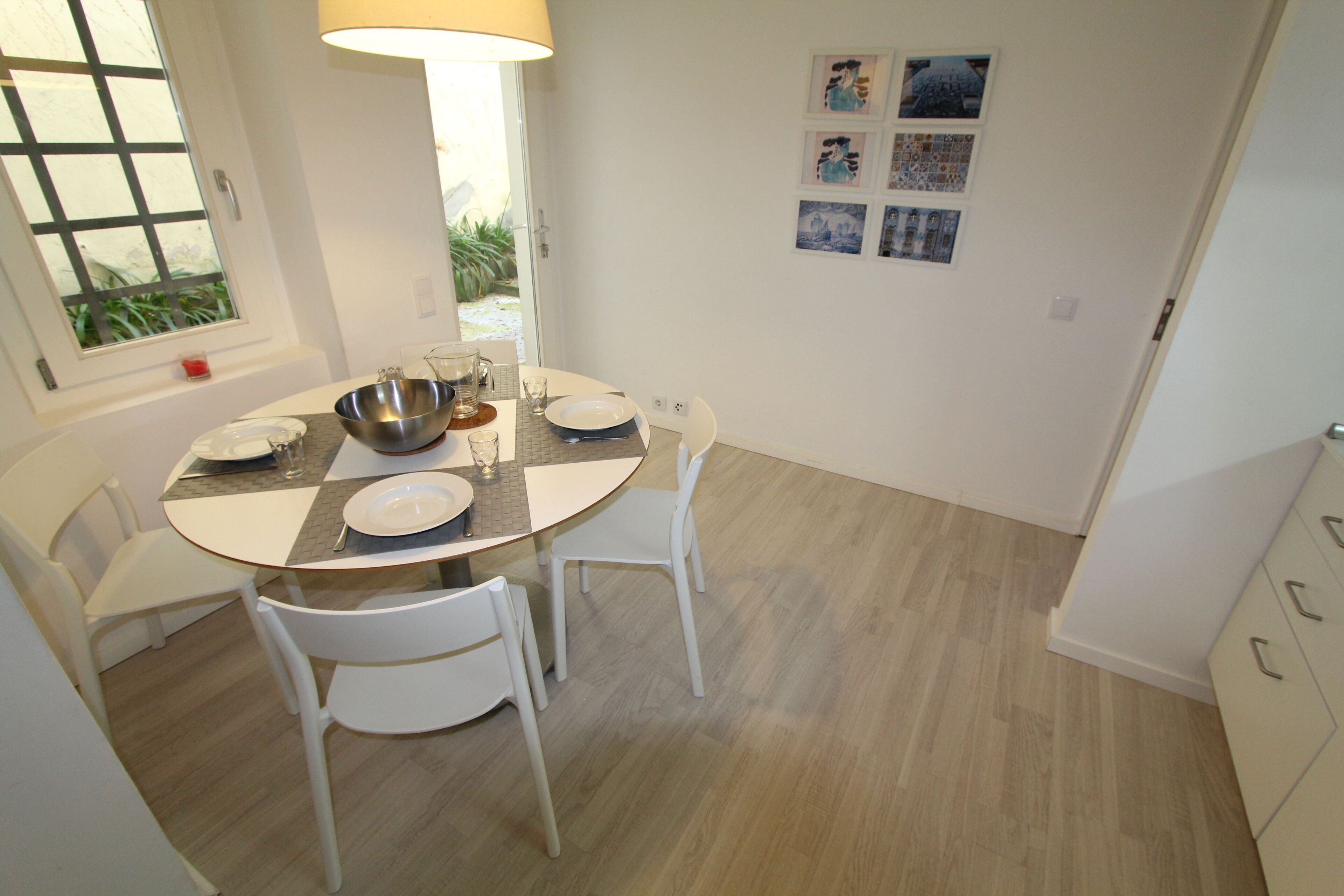 A dining area with a round table, white chairs, and a window with a view of greenery.