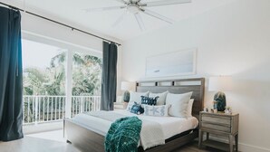 Un dormitorio con cama, mesitas de noche, ventilador de techo y vistas a la vegetación.