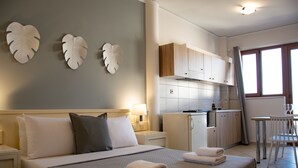 A hotel room with a bed, bedside tables, a desk, a chair, a kitchenette, and a window. - Horizon Apartments Platanias (Platanias)