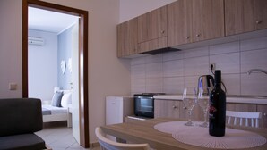A modern kitchen with wooden cabinets, a dining table with two chairs, and a small refrigerator. - Horizon Apartments Platanias (Platanias)