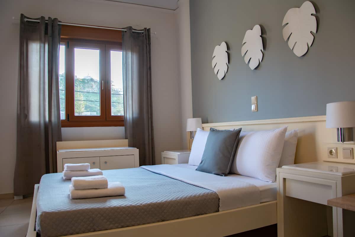Una cama bien hecha con toallas, una mesita de noche con una lámpara y una ventana con cortinas.