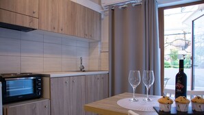 A kitchen with wooden cabinets, a built-in microwave, a dining table with a placemat, two wine glasses, and a bottle of wine. - Horizon Apartments Platanias (Platanias)