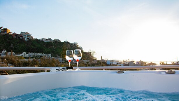 A hot tub with two glasses of wine on a balcony overlooking a hillside with houses. - Horizon Apartments Platanias (Platanias)