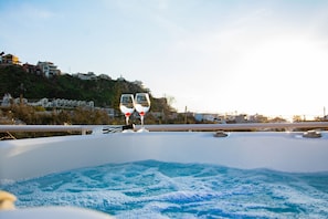 A hot tub with two glasses of wine on a balcony overlooking a hillside with houses. - Horizon Apartments Platanias (Platanias)