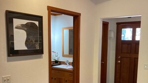 Ein Holzboden-Flur mit einem gerahmten Vogelbild, einem Spiegel und einer Tür zu einem Badezimmer.