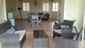 A living room with wicker furniture, a dining table with chairs, and a kitchen area in the background. - TropicalKaz Guadeloupe - Villa Sunset (Sainte Rose)