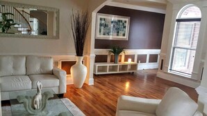 Een ruime woonkamer met een houten vloer, een witte bank, een glazen salontafel en een open haard.