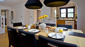 A dining area with a wooden table set for breakfast, including plates, cutlery, and a vase with flowers. - 3 bedroom accommodation in Wadebridge (Wadebridge)