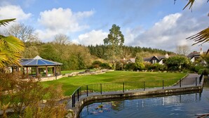 A tranquil garden with a pond, a gazebo, and a pathway leading to a cluster of houses. - 3 bedroom accommodation in Wadebridge (Wadebridge)