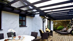 A covered patio with wicker furniture, a dining table with a white tablecloth, and a small garden area. - 3 bedroom accommodation in Wadebridge (Wadebridge)