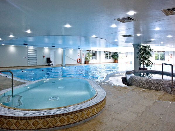 An indoor swimming pool with a hot tub, tiled flooring, and potted plants.