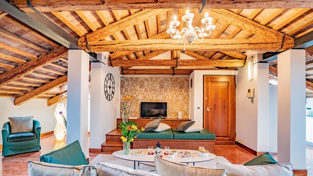 Ein gemütliches Zimmer mit Holzbalkendecke, einer Couch, einem Fernseher und einem Esstisch mit Speisen.
