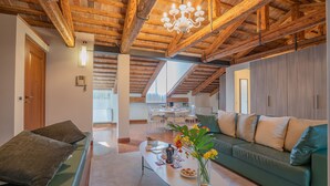 Ein geräumiger Wohnbereich mit hoher Holzbalkendecke, einem grünen Sofa, einem Couchtisch mit Snacks und einer Kristallleuchtre.