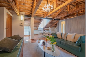 A spacious living area with a high wooden ceiling, a green sofa, a coffee table with snacks, and a chandelier.