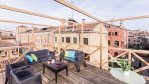 Eine Dachterrasse mit Holzbalken, einer Sofagarnitur, einem Tisch mit Getränken und einem Blumentopf.